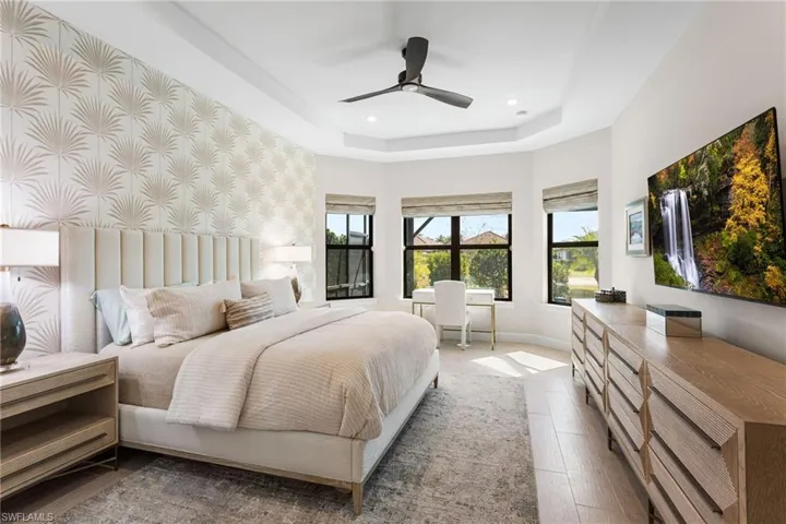 Bedroom with ceiling fan, a tray ceiling, wood finished floors, and an office area
