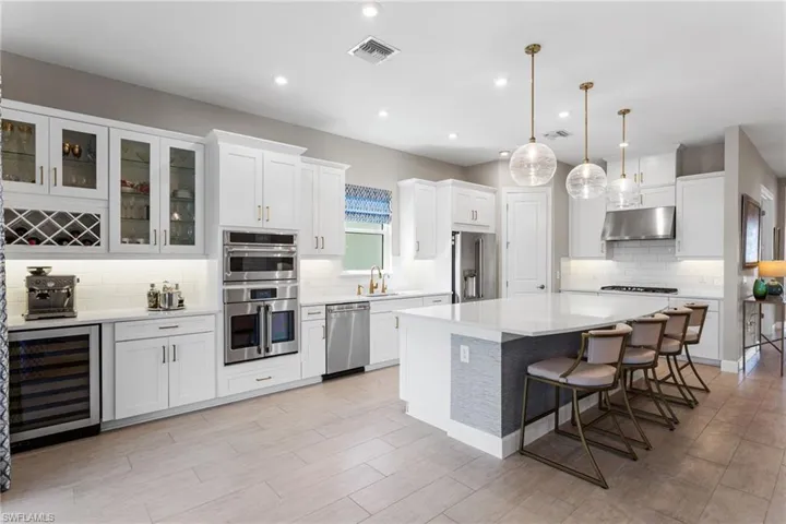 Kitchen with wine cooler, a kitchen bar, white cabinets, hanging light fixtures, and stainless steel appliances