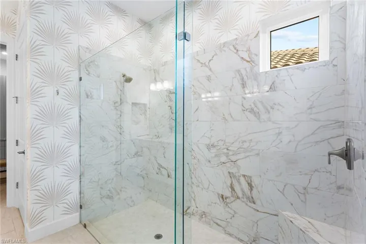 Bathroom with a marble finish shower and wallpapered walls