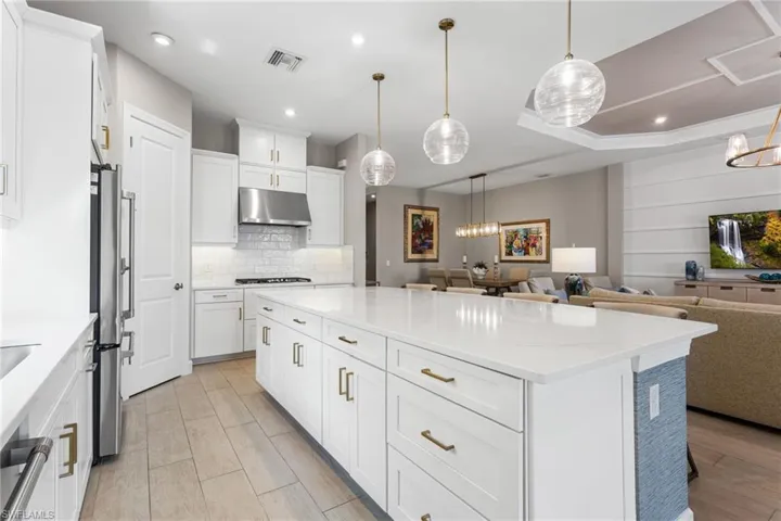 Kitchen featuring a center island, open floor plan, white cabinets, light stone countertops, and suspended lighting