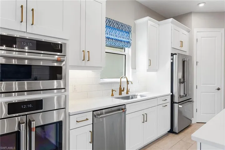 Kitchen with stainless steel appliances, white cabinetry, light stone countertops, and tasteful backsplash