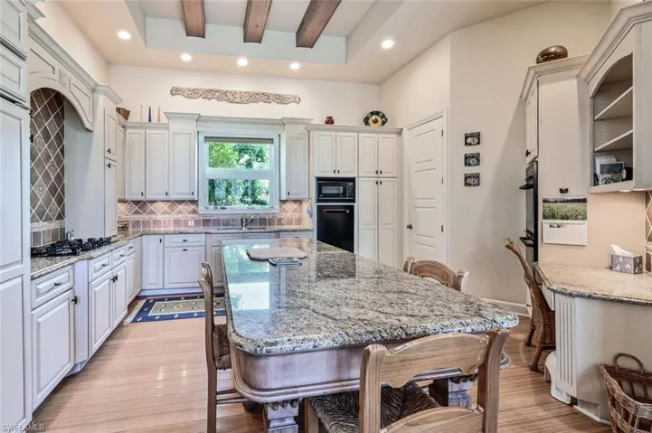 Kitchen with white cabinetry, black appliances, a kitchen bar, and light stone countertops