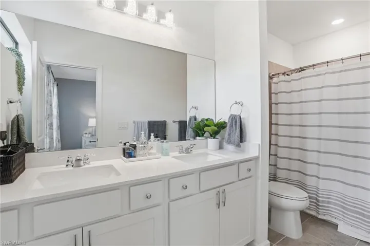Double vanity with integrated sinks, white cabinetry, chrome hardware, and a large wall-mounted mirror
