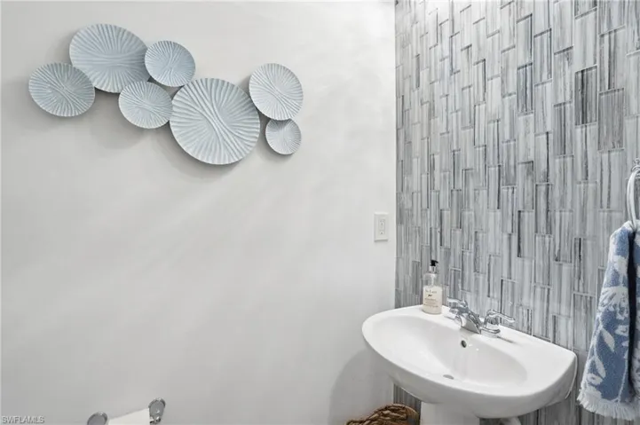 Downstairs half bath/powder room with pedestal sink with chrome faucet, upgraded glass waterfall tile wall, and light-toned painted walls