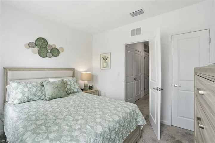 Bedroom featuring light gray carpeting, crisp white walls, a multi-paneled white door, and a built-in closet with bifold doors