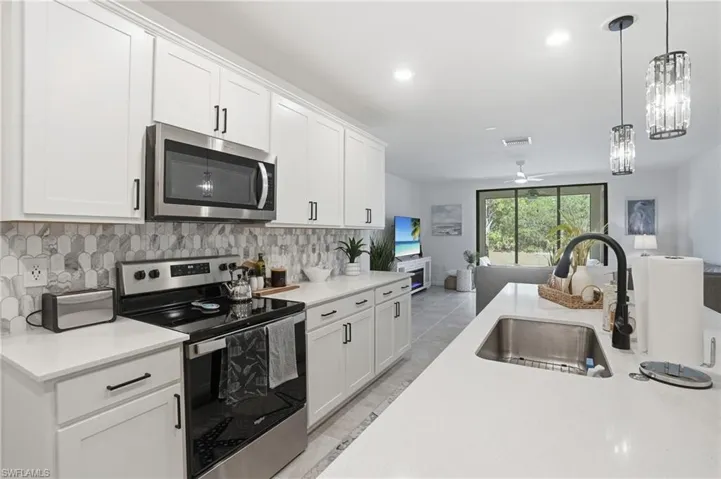Modern kitchen featuring white shaker cabinetry, stainless steel appliances, upgraded patterned tile backsplash, white countertops, and an undermount sink with a black gooseneck faucet