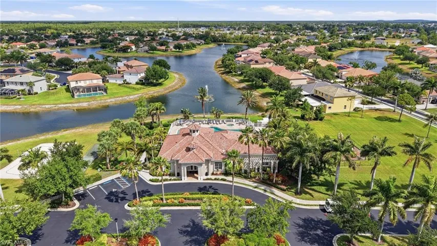 Community clubhouse featuring a red tile roof and swimming pool, surrounded by mature palm trees and lush landscaping