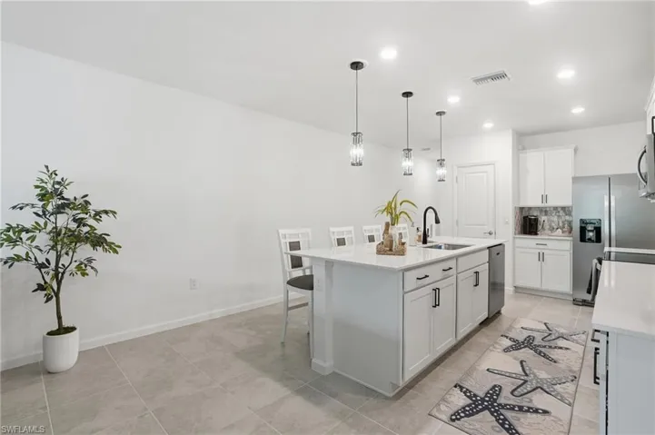 Contemporary kitchen featuring a large center island with integrated sink, white cabinetry, stainless steel appliances, recessed lighting, and upgraded pendant fixtures