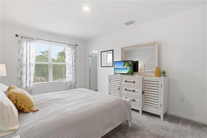 Bright interior space featuring a window with horizontal blinds and decorative curtains, recessed ceiling lighting, light gray carpet, and white painted walls