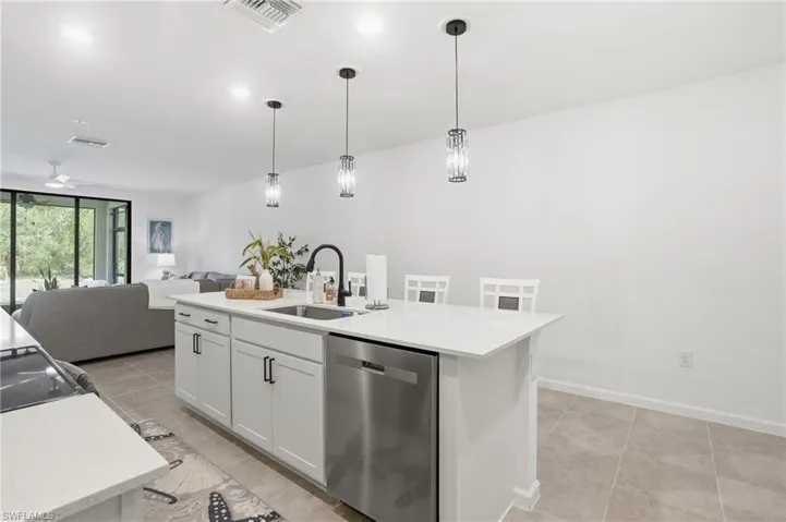 Kitchen island with white cabinetry, stainless steel dishwasher, and quartz-finish countertop, upgraded pendant lighting fixtures.