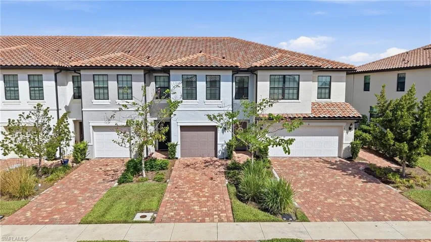 Mediterranean-style townhome featuring a tile roof, stucco exterior, black-framed windows, paver driveway, and an attached garage
