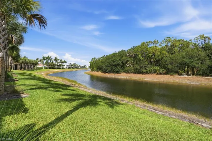 Waterfront property, expansive green lawn, mature palm trees, and lush natural vegetation