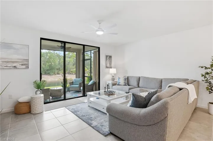 Expansive living area with large format tile flooring, a ceiling fan, and sliding glass doors opening to a screened lanai
