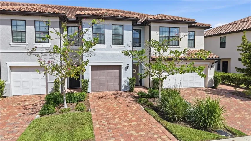 Mediterranean-style facade featuring a red tile roof, stucco exterior, multiple windows with black trim, an integrated garage, and a paver driveway