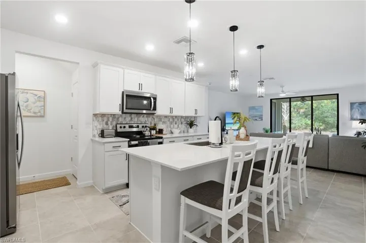 Modern kitchen featuring white shaker cabinetry, stainless steel appliances, an upgraded tile backsplash, and a spacious island with upgraded pendant lighting