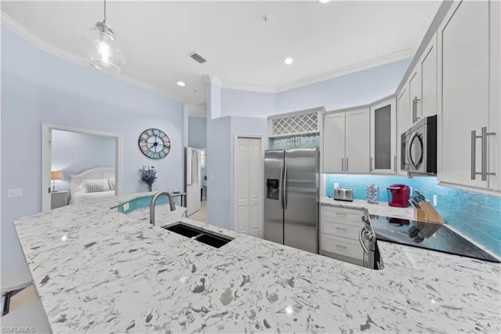 Kitchen with light stone counters, appliances with stainless steel finishes, decorative light fixtures, ornamental molding, and glass insert cabinets