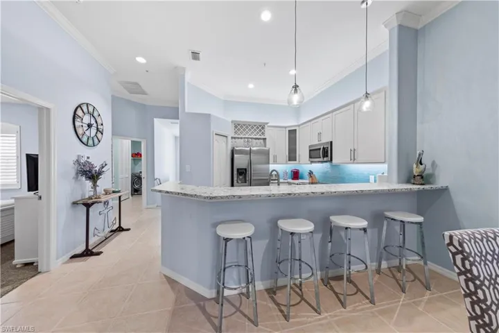 Kitchen with a kitchen breakfast bar, light tile patterned floors, a peninsula, ornamental molding, and stainless steel appliances