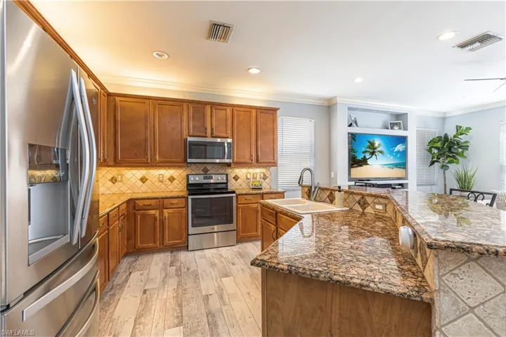 Kitchen with stainless steel appliances, brown cabinetry, a sink, and visible vents