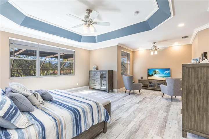 Bedroom featuring a tray ceiling, light wood finished floors, visible vents, ornamental molding, and baseboards