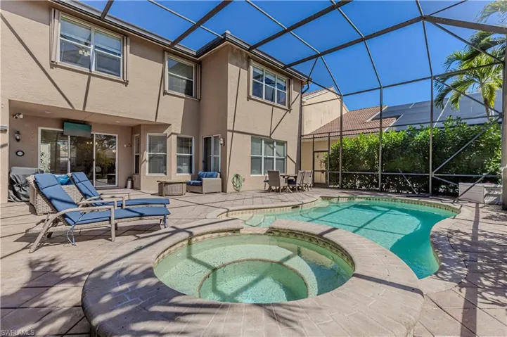 View of pool with glass enclosure, a pool with connected hot tub, and a patio