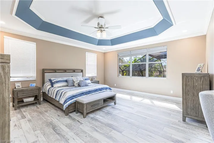 Bedroom featuring a ceiling fan, ornamental molding, a raised ceiling, and wood finished floors
