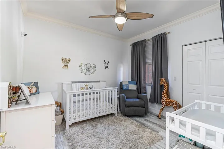 Bedroom featuring a closet, ornamental molding, ceiling fan, wood finished floors, and a nursery area