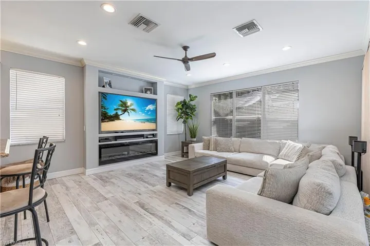 Living area with light wood-type flooring, ceiling fan, visible vents, and crown molding