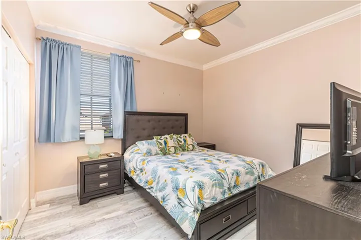 Bedroom with ornamental molding, light wood-type flooring, a ceiling fan, and baseboards