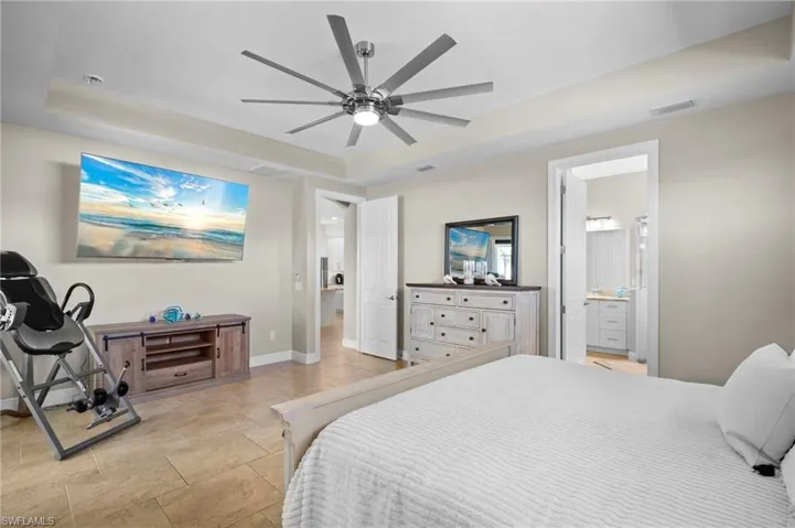 Bedroom featuring a raised ceiling, a ceiling fan, and ensuite bath