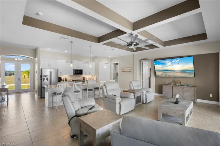 Living room with arched walkways, coffered ceiling, light tile patterned floors, french doors, and beamed ceiling