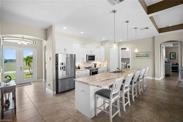 Kitchen with arched walkways, a kitchen breakfast bar, stainless steel appliances, white cabinetry, and a large island with sink