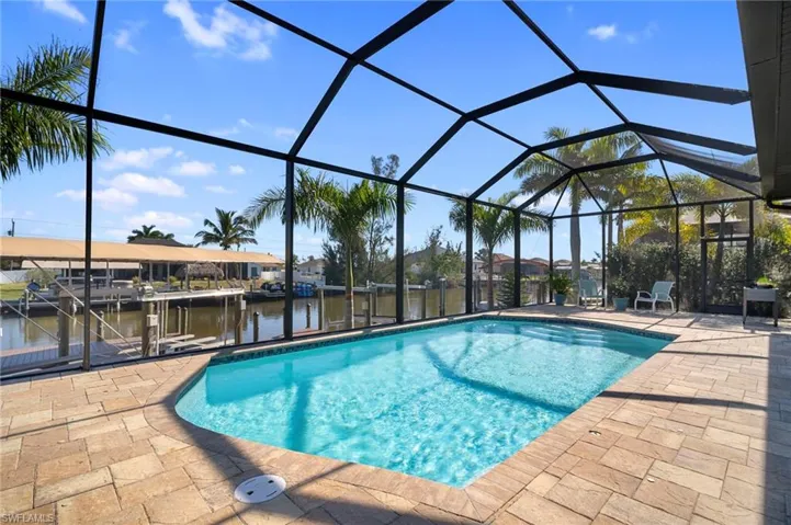 Outdoor pool with glass enclosure, a sunroom, a patio area, a water view, and a dock
