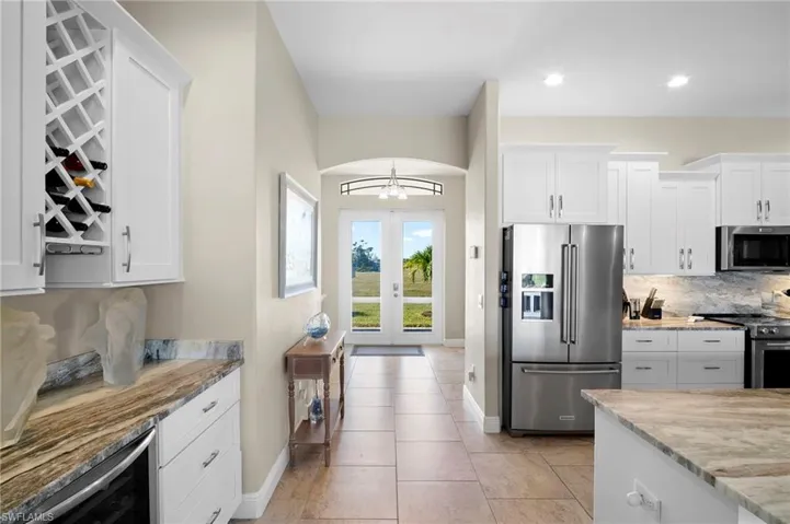 Kitchen with appliances with stainless steel finishes, backsplash, white cabinetry, light stone countertops, and wine cooler