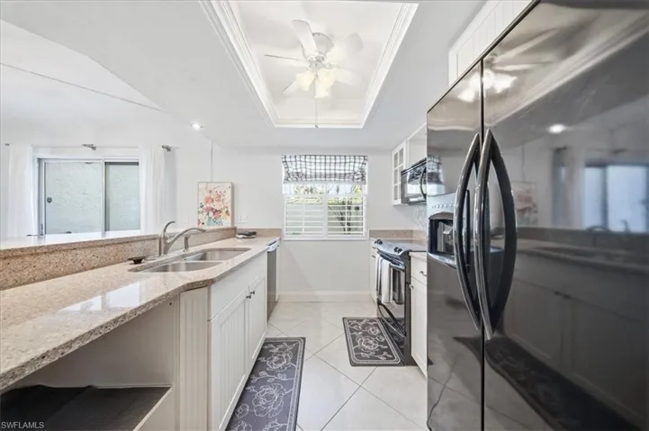 Kitchen featuring black appliances, white cabinets, a tray ceiling, light stone counters, and light tile patterned flooring