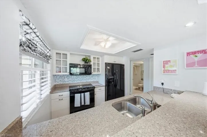 Kitchen featuring white cabinets, black appliances, glass insert cabinets, light stone countertops, and backsplash