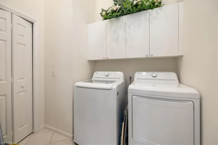 Laundry area featuring light tile patterned floors, washing machine and clothes dryer, and cabinets