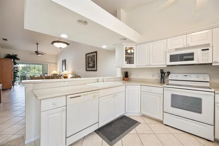 Kitchen with ceiling fan, white cabinets, kitchen peninsula, white appliances, and vaulted ceiling