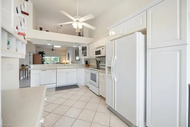 Kitchen with high vaulted ceiling, white appliances, ceiling fan, and white cabinetry