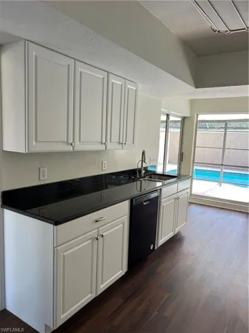 Kitchen with dishwashing machine, dark wood-type flooring, white cabinetry, and dark countertops