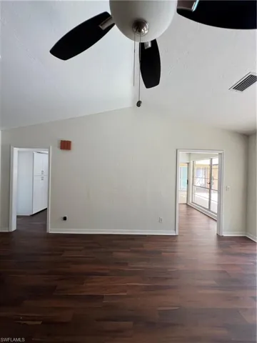 Empty room featuring vaulted ceiling, dark wood-style floors, and a ceiling fan
