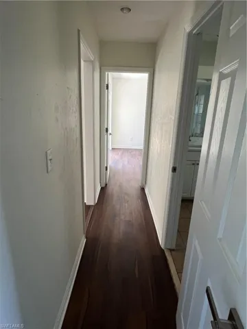 Corridor with dark wood-type flooring and baseboards