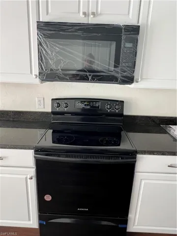 Kitchen view of black range with electric stovetop, dark countertops, and white cabinets