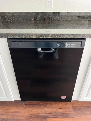 Detailed view of black dishwasher, dark countertops, and wood finished floors
