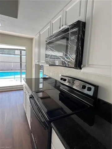 Kitchen featuring range, white cabinetry, dark wood-style flooring, dark countertops, and a textured ceiling