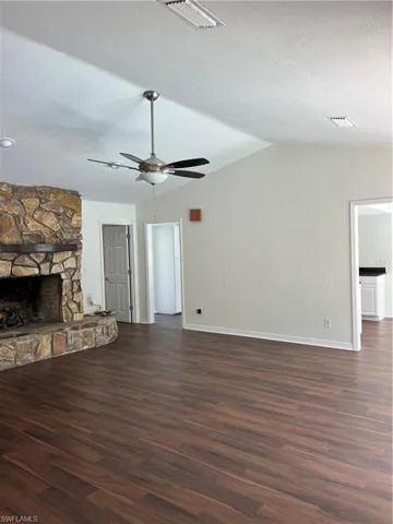 Unfurnished living room featuring ceiling fan, dark wood finished floors, vaulted ceiling, a stone fireplace, and a textured ceiling