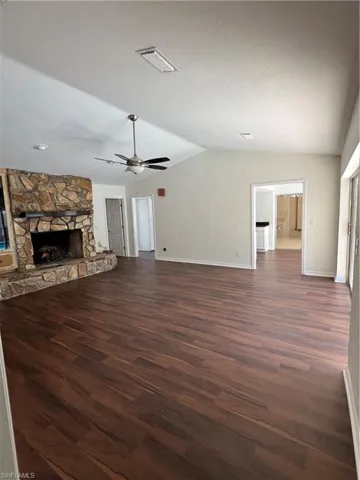 Unfurnished living room with lofted ceiling, a fireplace, dark wood-type flooring, and ceiling fan