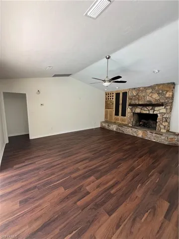 Unfurnished living room with dark wood-type flooring, a fireplace, a ceiling fan, and vaulted ceiling