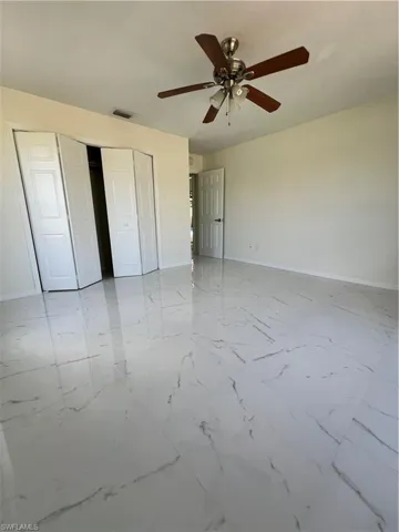 Unfurnished bedroom featuring a closet, light marble finish flooring, and ceiling fan