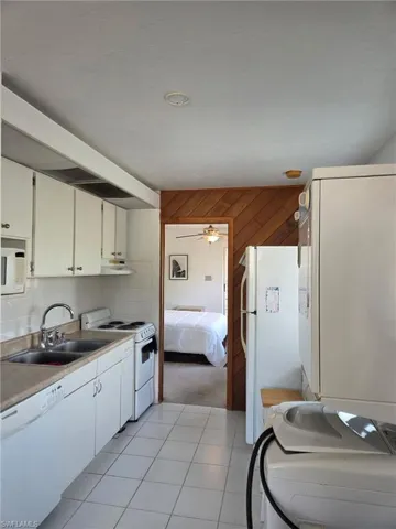 Kitchen with white appliances, light tile patterned floors, light countertops, backsplash, and white cabinets