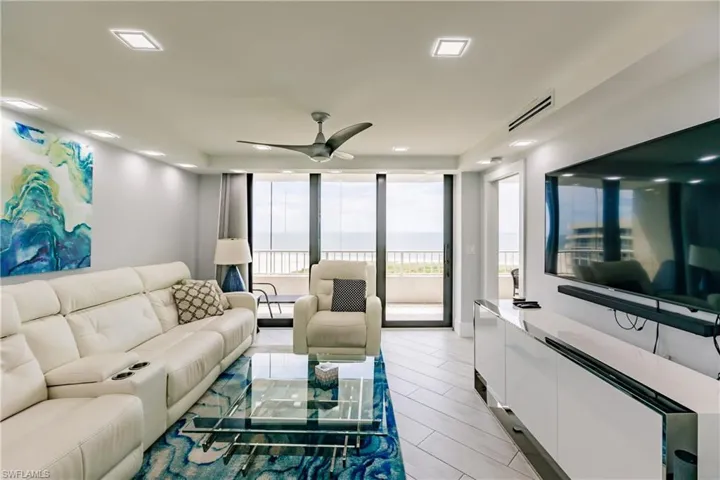 Living room with a ceiling fan, floor to ceiling windows, and wood tiled floors